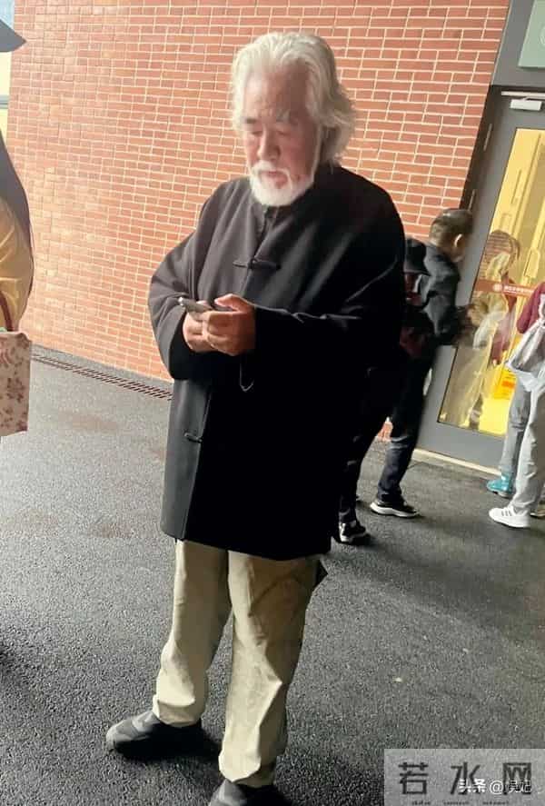 75岁张纪中现身浙江医院急诊门口,他站着看手机,表情凝重。