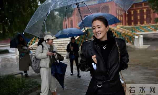 59岁巩俐现身北京公园，穿黑皮衣配透明伞，雨中喝酸奶吃冰糖葫芦
