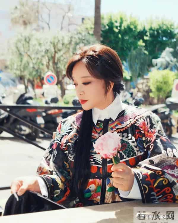 刘晓庆真的不服老啊，身穿黑色花纹袍子，头上别着几朵鲜花